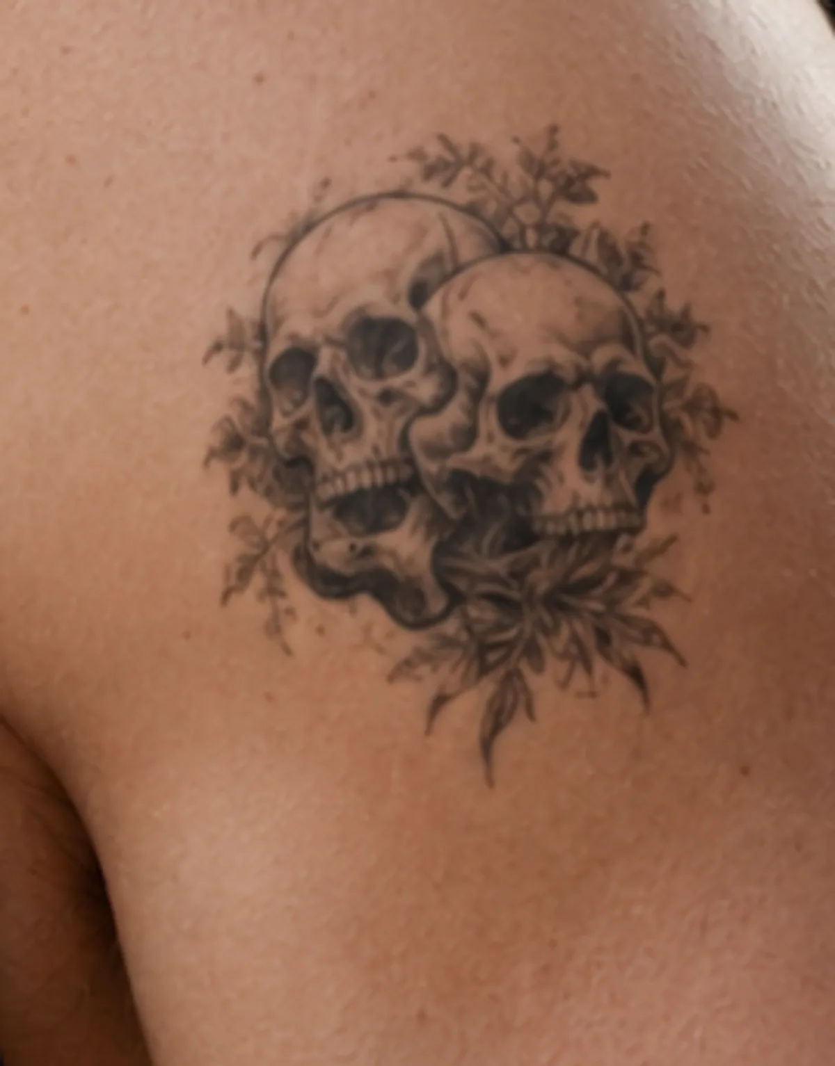 Black & grey-tatuering av dödskallar med blommor på rygg — innan laserbehandling